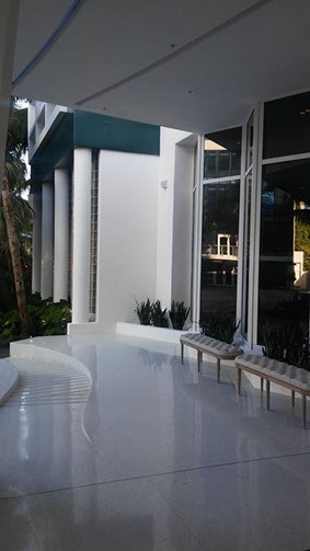 A white patio with benches and plants outside.