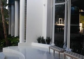 A white patio with benches and plants outside.